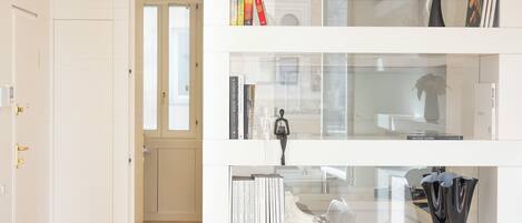 Un interior moderno con una puerta blanca, un pasillo y una vitrina de vidrio con libros y objetos decorativos.