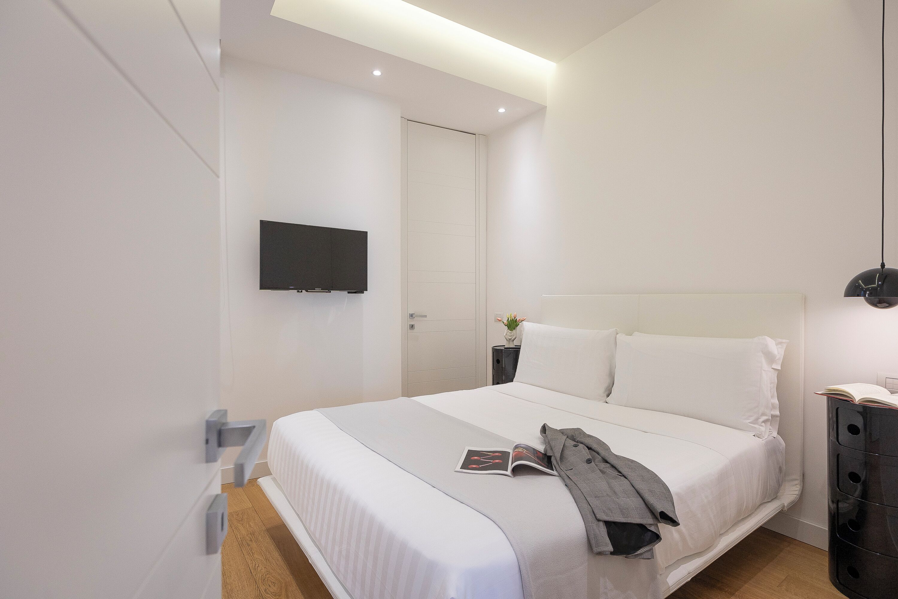 Une chambre d’hôtel moderne avec un grand lit, un téléviseur à écran plat fixé au mur et une table de chevet avec une lampe.