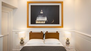 A hotel room with a bed, two bedside tables with lamps, a framed picture of a building, and a window with a view of a dome structure. - Amazing Vittoriano (Rome)