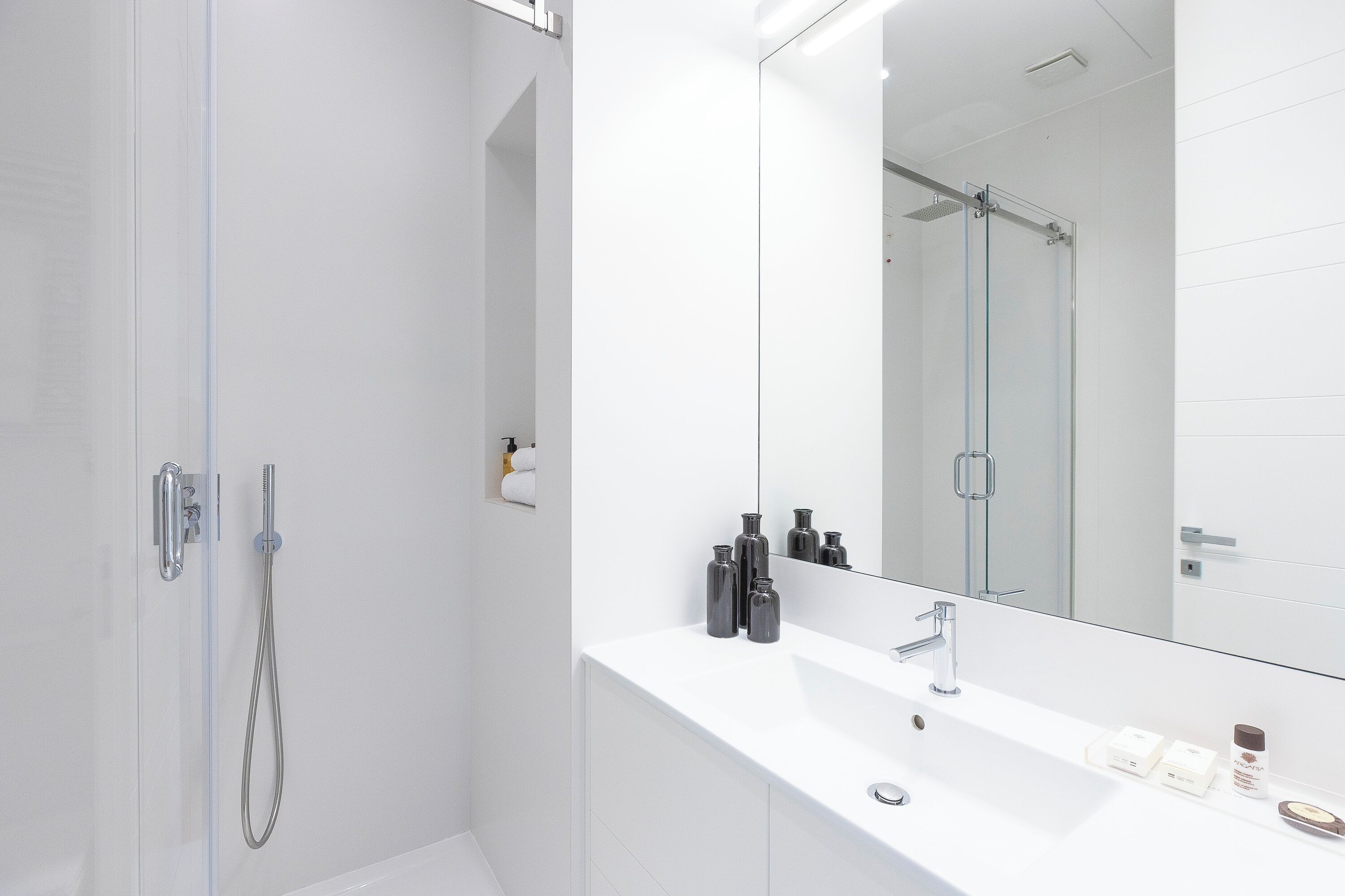 A modern bathroom with a glass-enclosed shower, a white sink, and a large mirror.