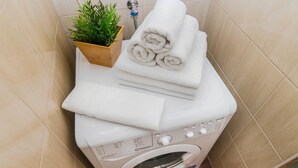 A washing machine with folded towels on top, a potted plant, and a faucet in a bathroom with beige tiles. - APT Prague Ch. Bridge by Michal&Friends (Prague)