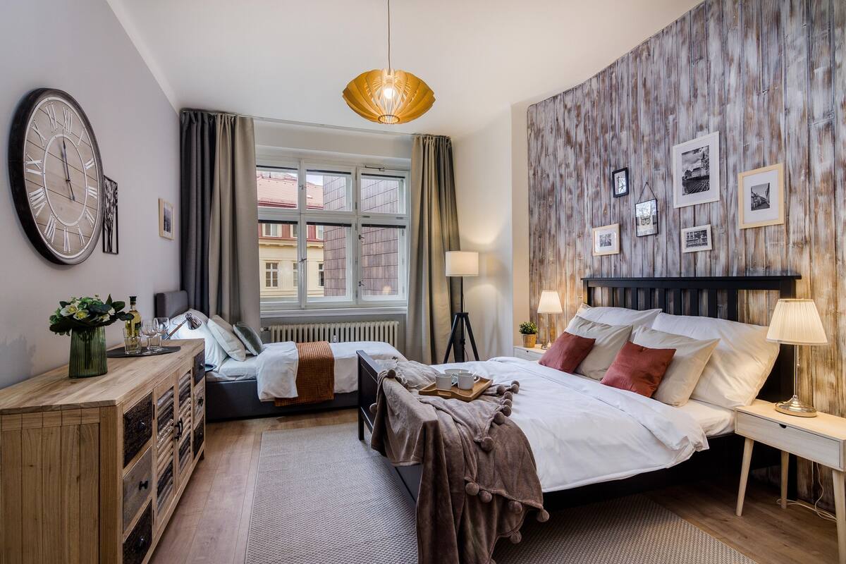 A well-lit bedroom with a large bed, bedside tables, a dresser, and a window with curtains.