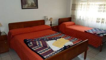 Habitación de hotel con dos camas, cada una con una colcha roja y una manta estampada. Hay una mesita de noche con una lámpara y un teléfono en la pared.