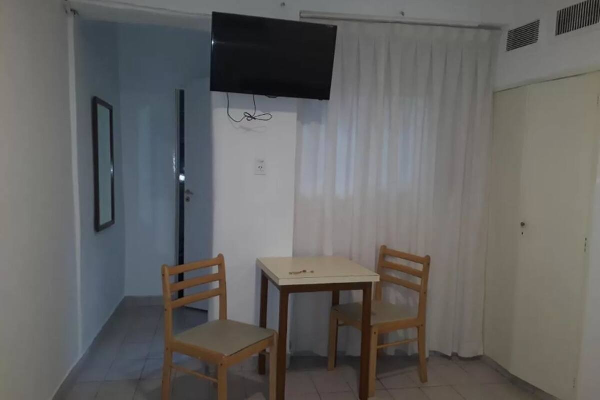 A small room with a table and two chairs, a television mounted on the wall, and a door with a curtain.