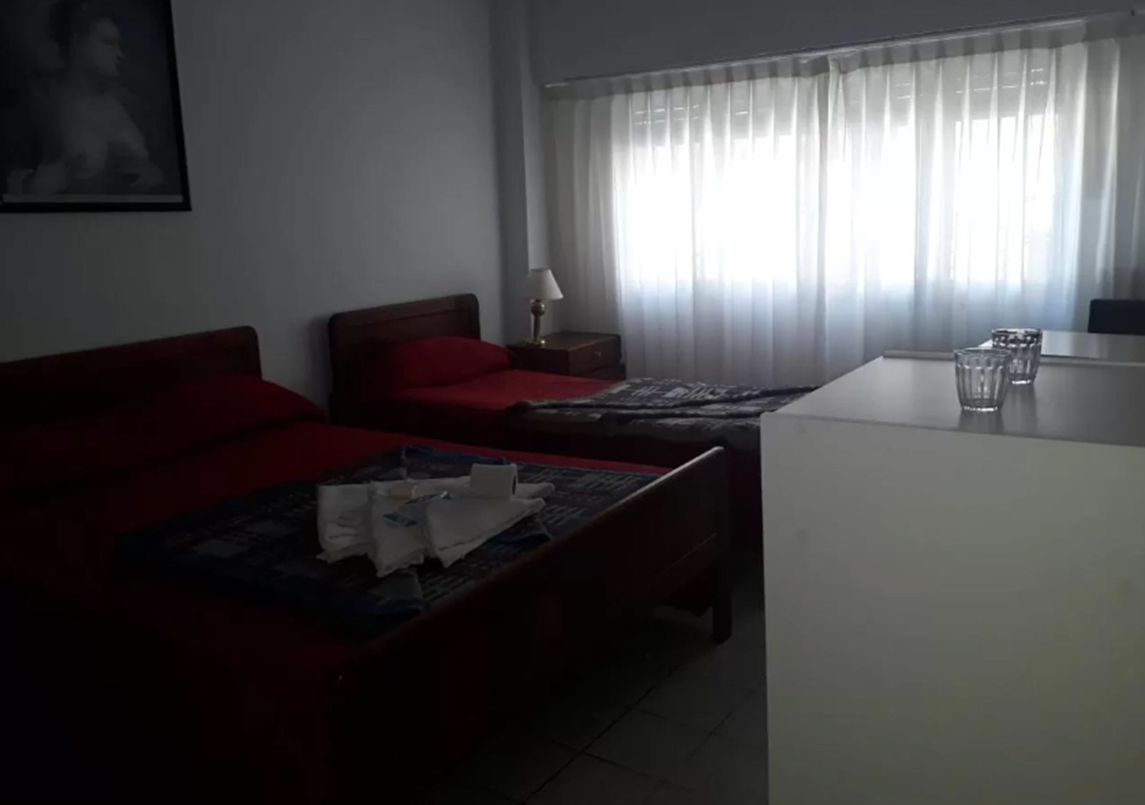 Een hotelkamer met twee enkele bedden, een kleine tafel met glazen en een raam met dunne gordijnen.