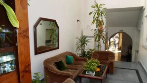A cozy living area with a brown sofa, a matching armchair, and a coffee table. There are several potted plants and a large mirror on the wall. - Hotel San Carlos (Buenos Aires)