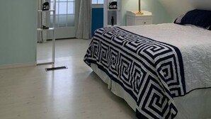 A bedroom with a bed, a nightstand, a lamp, and a window with curtains. - Sea-Breeze Cottage perched on the edge of the bay. (Eastport)