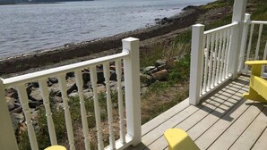 A wooden deck with white railings overlooking a rocky shoreline and calm water. - Sea-Breeze Cottage perched on the edge of the bay. (Eastport)