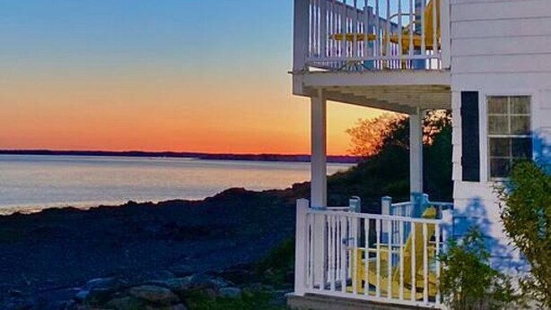 A two-story house with a balcony, located near a body of water. - Sea-Breeze Cottage perched on the edge of the bay. (Eastport)
