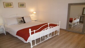 A neatly made bed with a white metal frame, a red blanket, and two pillows. There is a bedside table with a lamp, and a large mirror on the wall. - 4 The Courtyard Award Winning 4 Star Vineyard Gite (Monbadon)