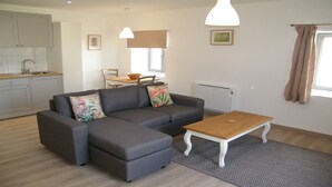 A modern living room with a grey sofa, a wooden coffee table, and a kitchen in the background. - 4 The Courtyard Award Winning 4 Star Vineyard Gite (Monbadon)