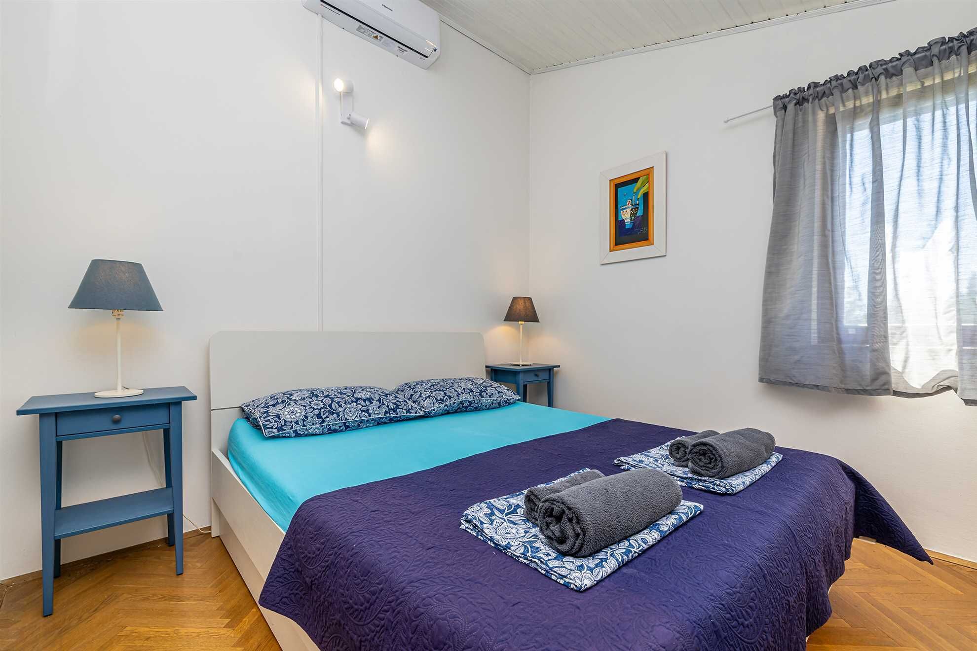 Ein Schlafzimmer mit einem Bett, zwei Nachttischen, einer Lampe, einem Bild an der Wand und einem Fenster mit Vorhängen.