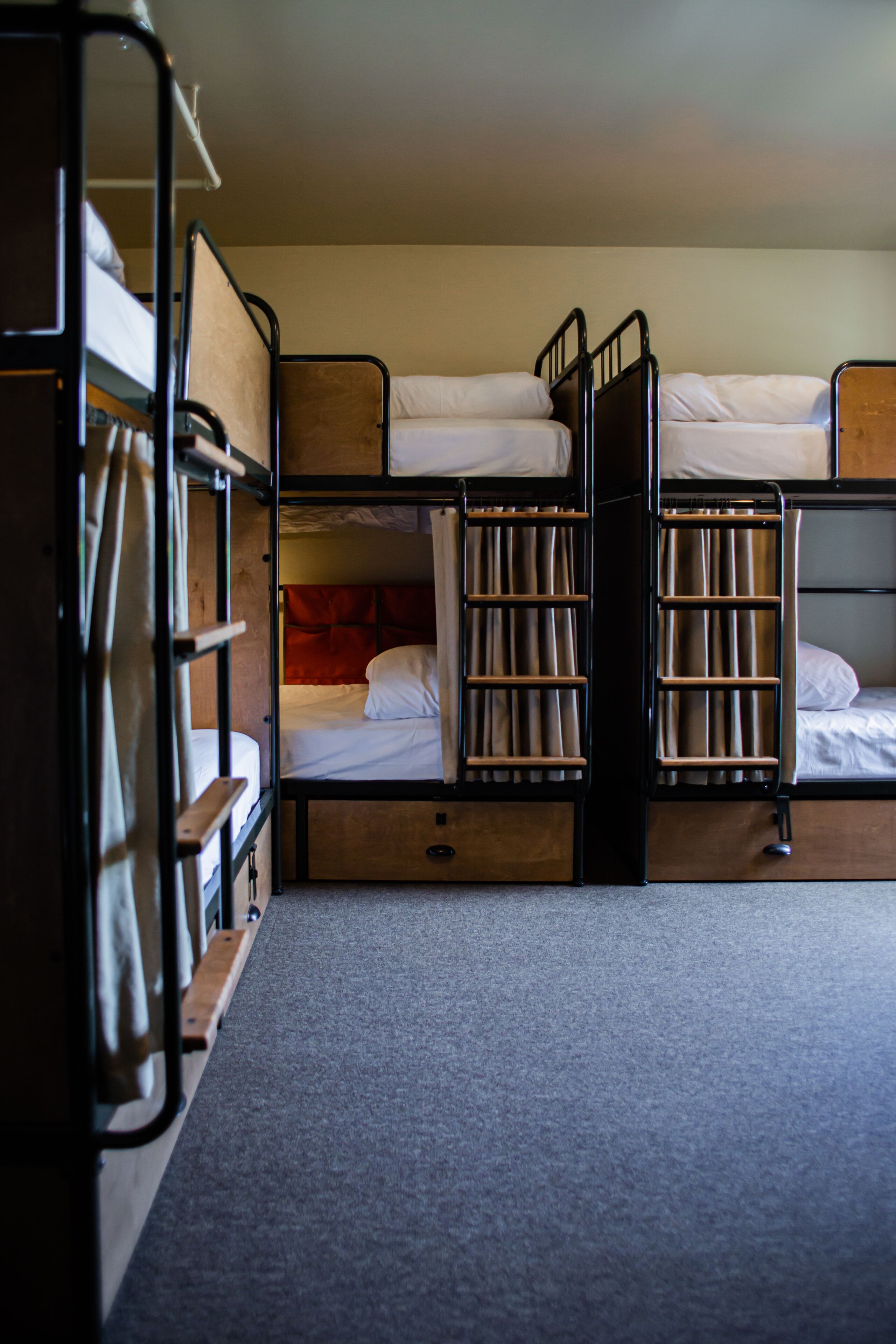A dormitory-style room with bunk beds, a small wooden desk, and a carpeted floor.