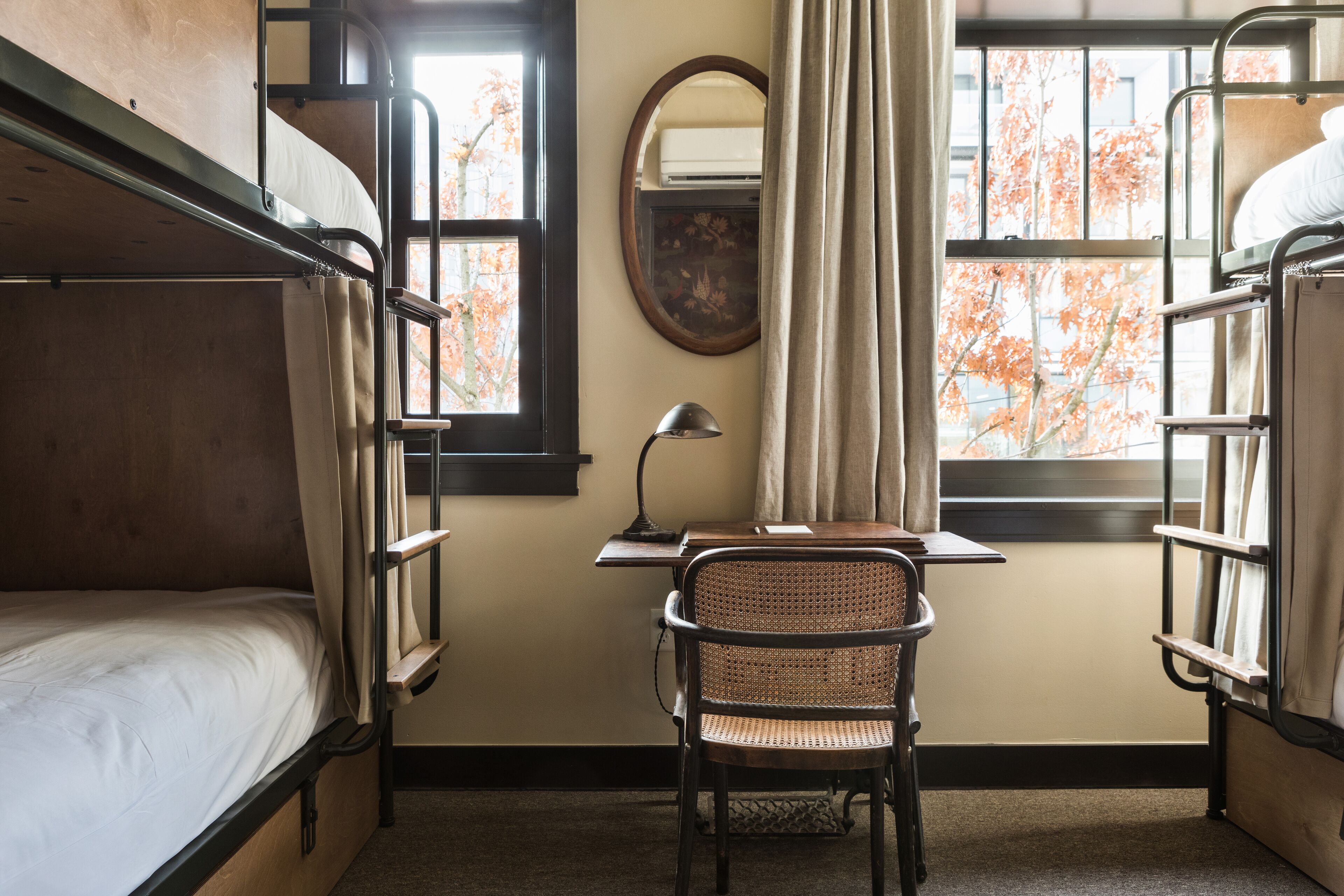 A bunk room with a desk, chair, and a window with autumn leaves.