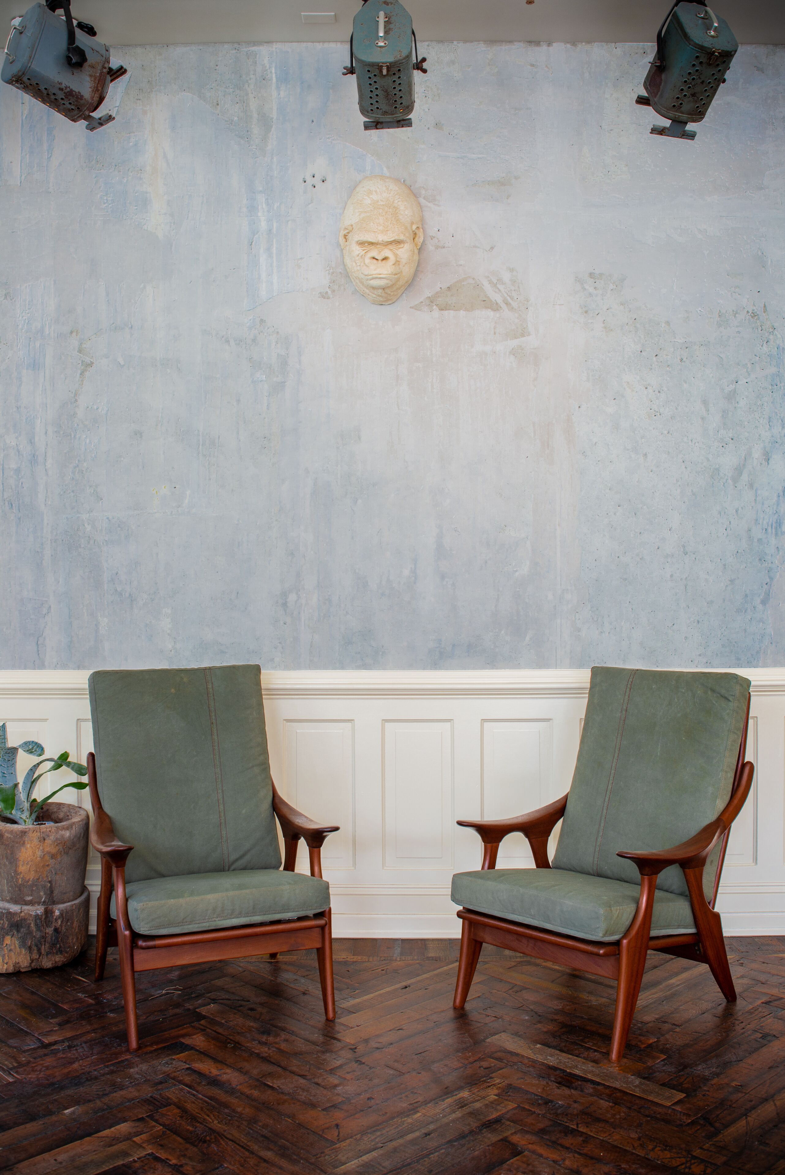Deux fauteuils verts, recouverts de tissu, avec des armatures en bois, un appui-tête en pierre fixé au mur et une plante en pot, à gauche.