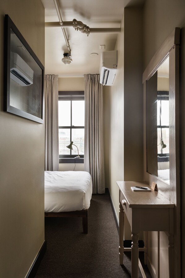 A hotel room with a bed, a desk, a mirror, and a window with curtains.