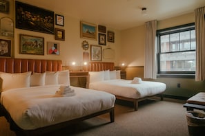 A hotel room with two beds, a large window, and various framed pictures on the wall.