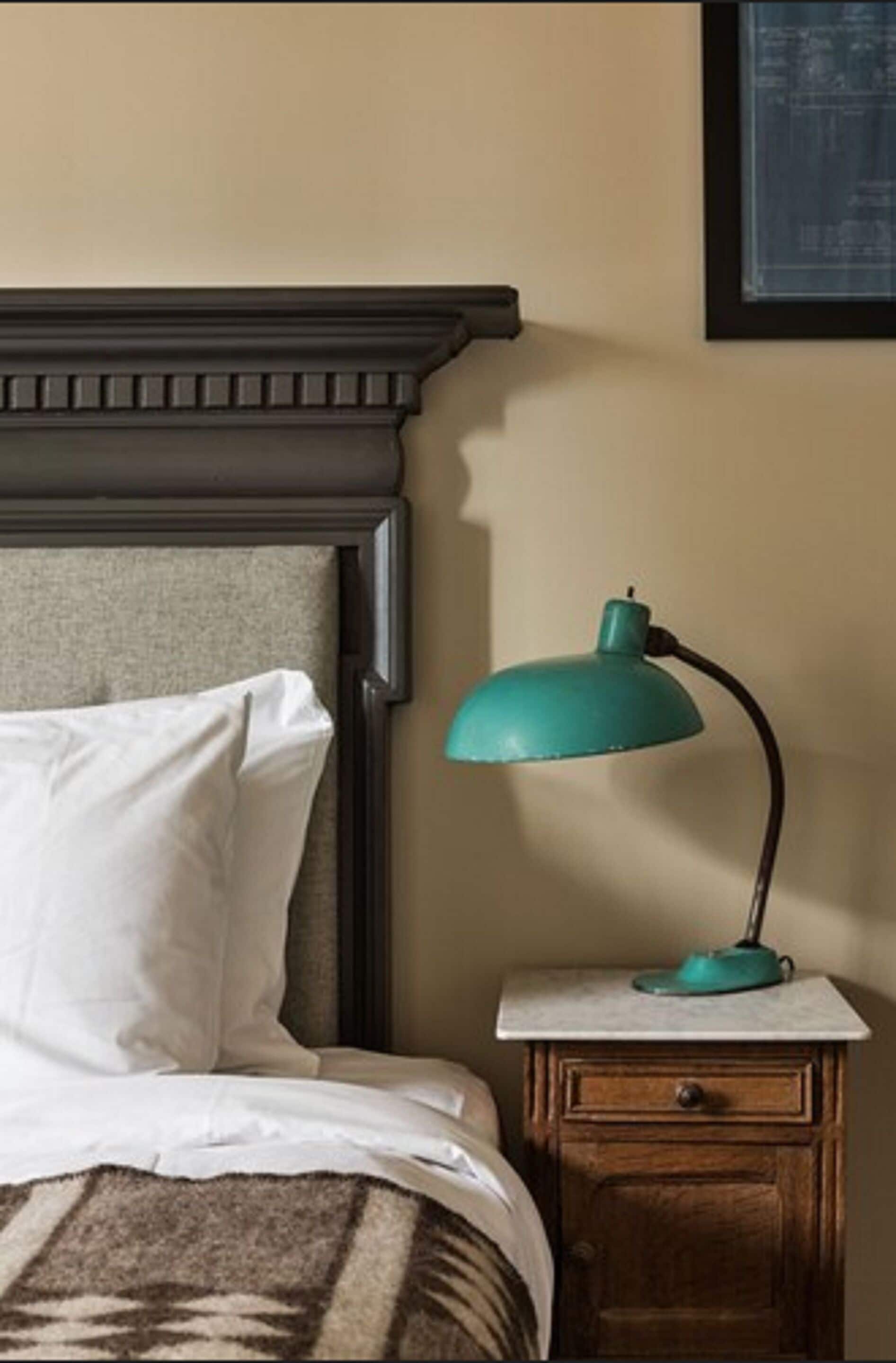 A bedroom with a bed, a nightstand, and a teal desk lamp.
