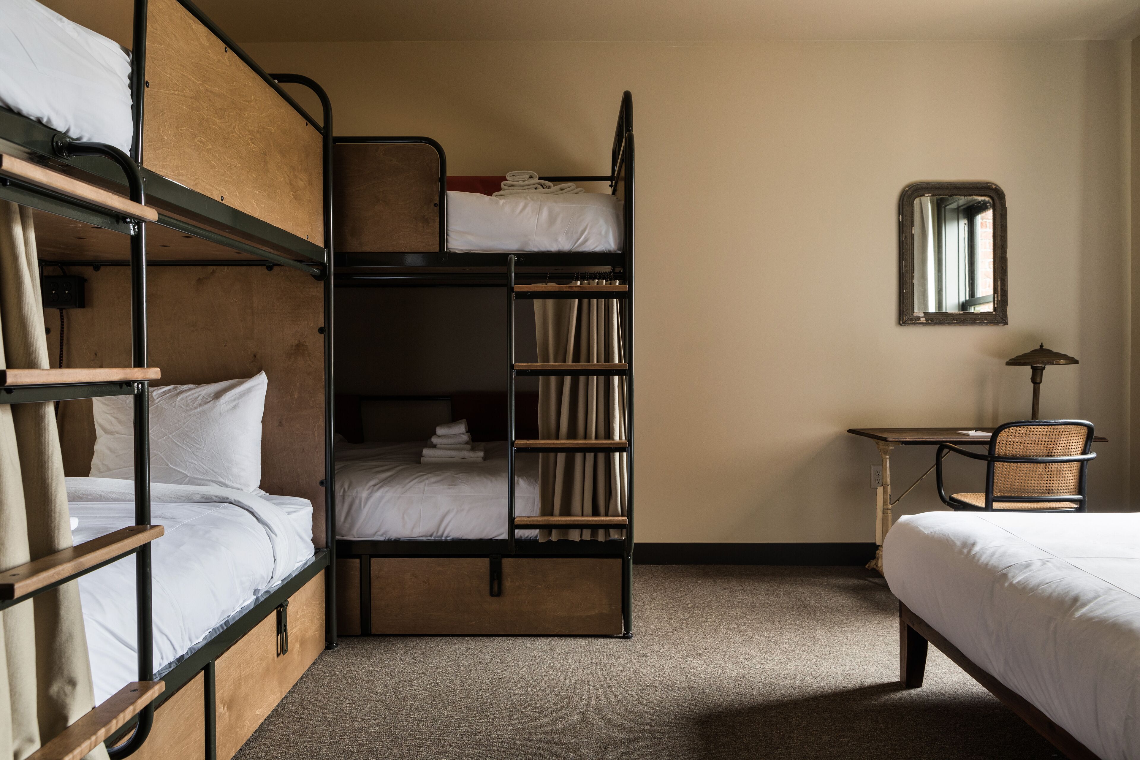 Een slaapkamer met een stapelbed, bureau en stoel, een spiegel en een raam.