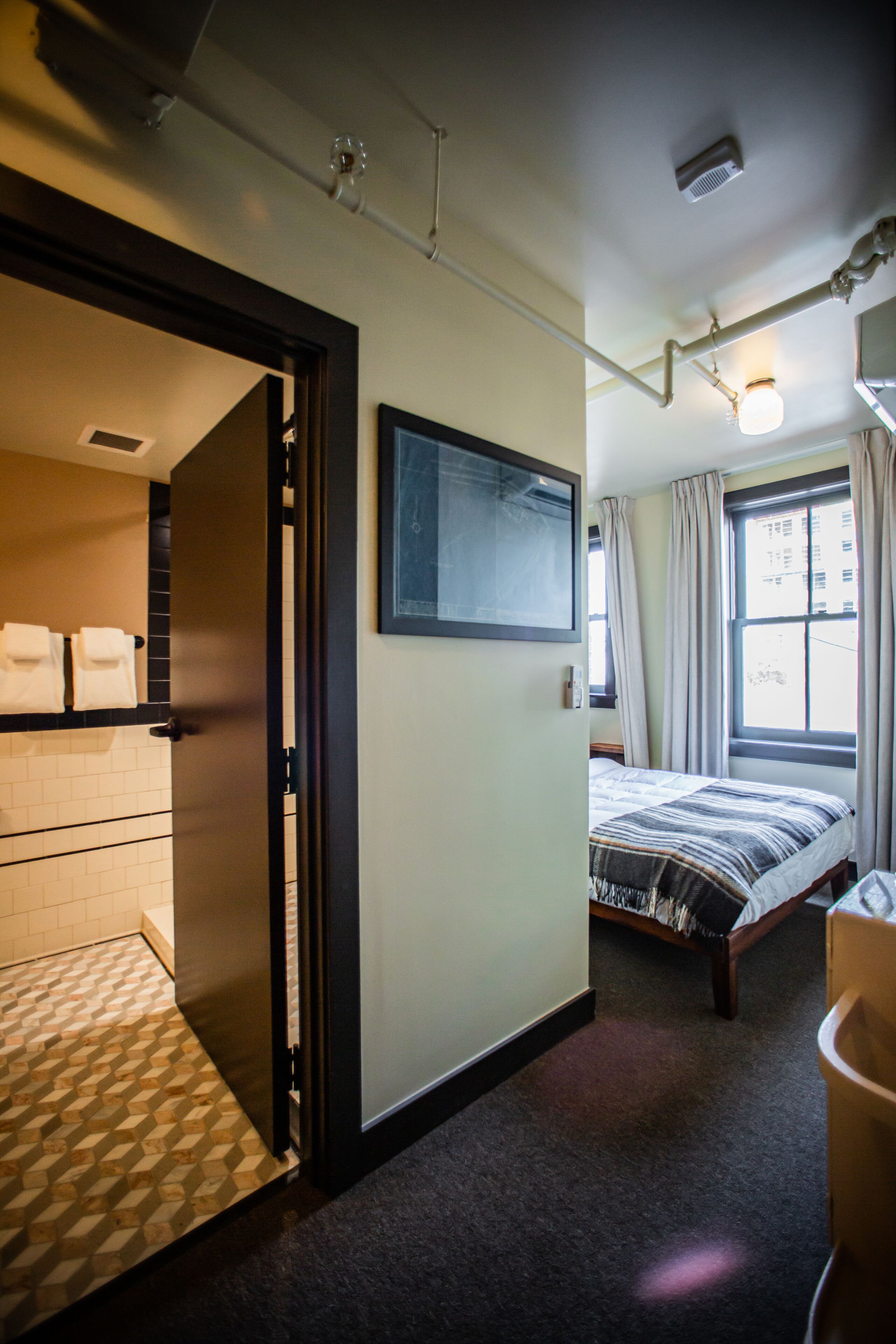Une chambre d’hôtel avec un lit, une salle de bain comprenant des toilettes et un lavabo, et une fenêtre avec des rideaux.