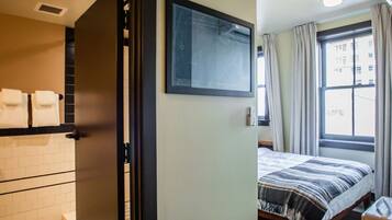 Une chambre d’hôtel avec un lit, une salle de bain comprenant des toilettes et un lavabo, et une fenêtre avec des rideaux.