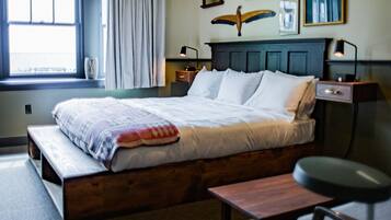 A bedroom with a bed, bedside tables, a window with curtains, and wall-mounted artwork.