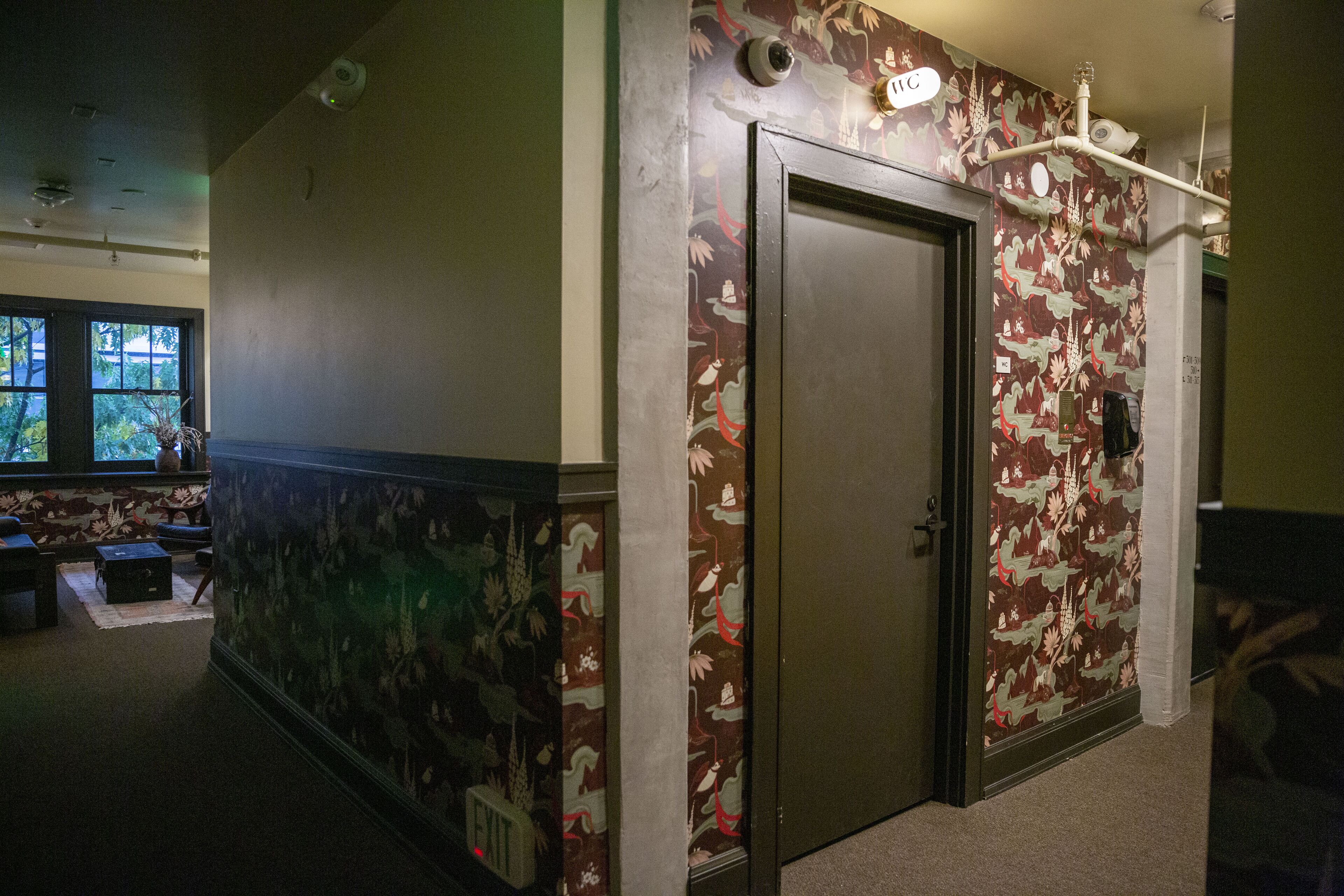 A hallway with a door, patterned wallpaper, and a window with a view of trees.