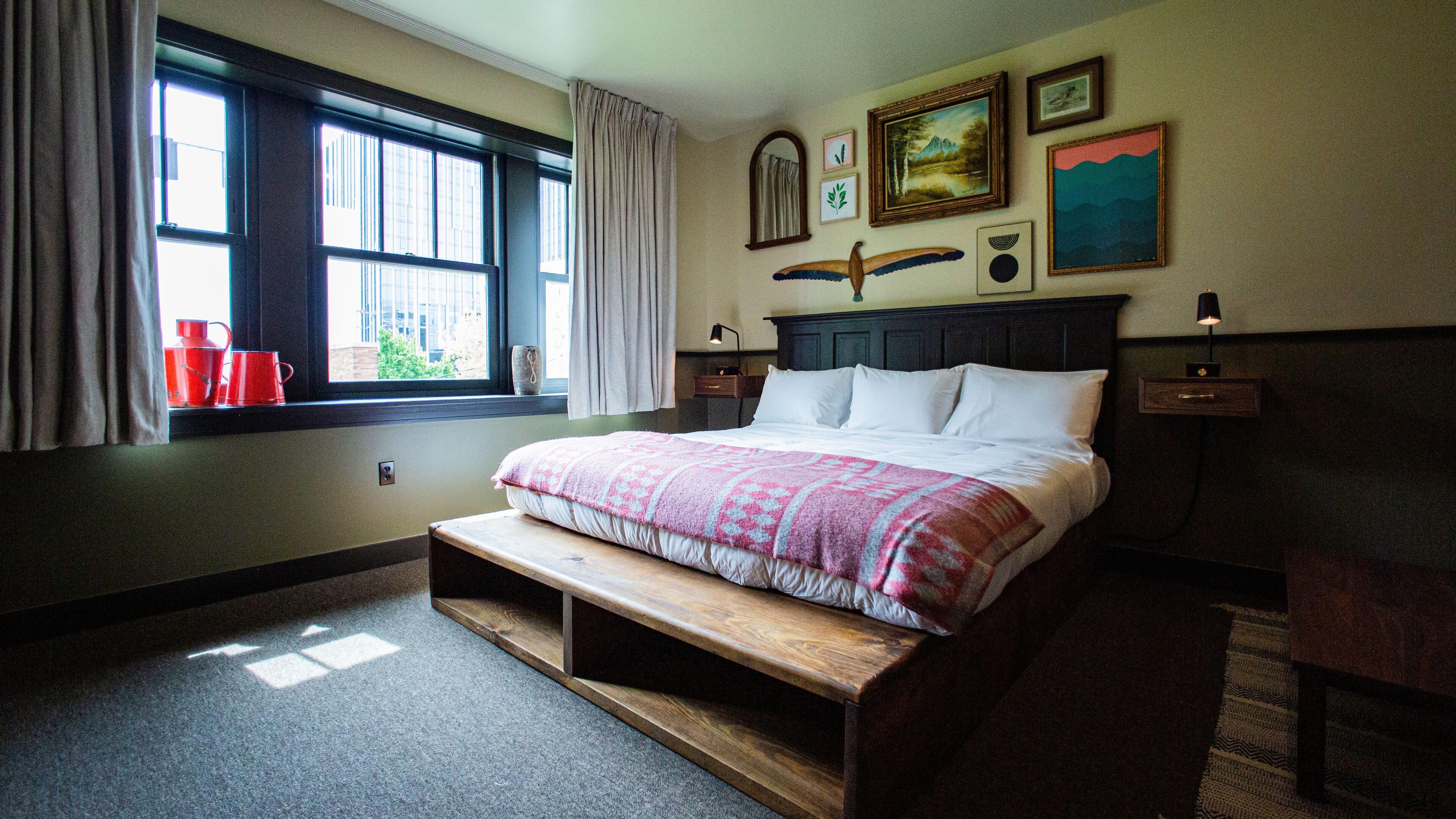 Um quarto com uma cama grande, uma janela com cortinas, uma mesa de cabeceira e um criado-mudo.