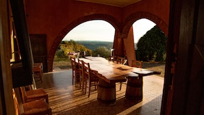 An outdoor dining area with a large wooden table and chairs, brick arches, and a view of the landscape. - Le Roghete (Acquapendente)