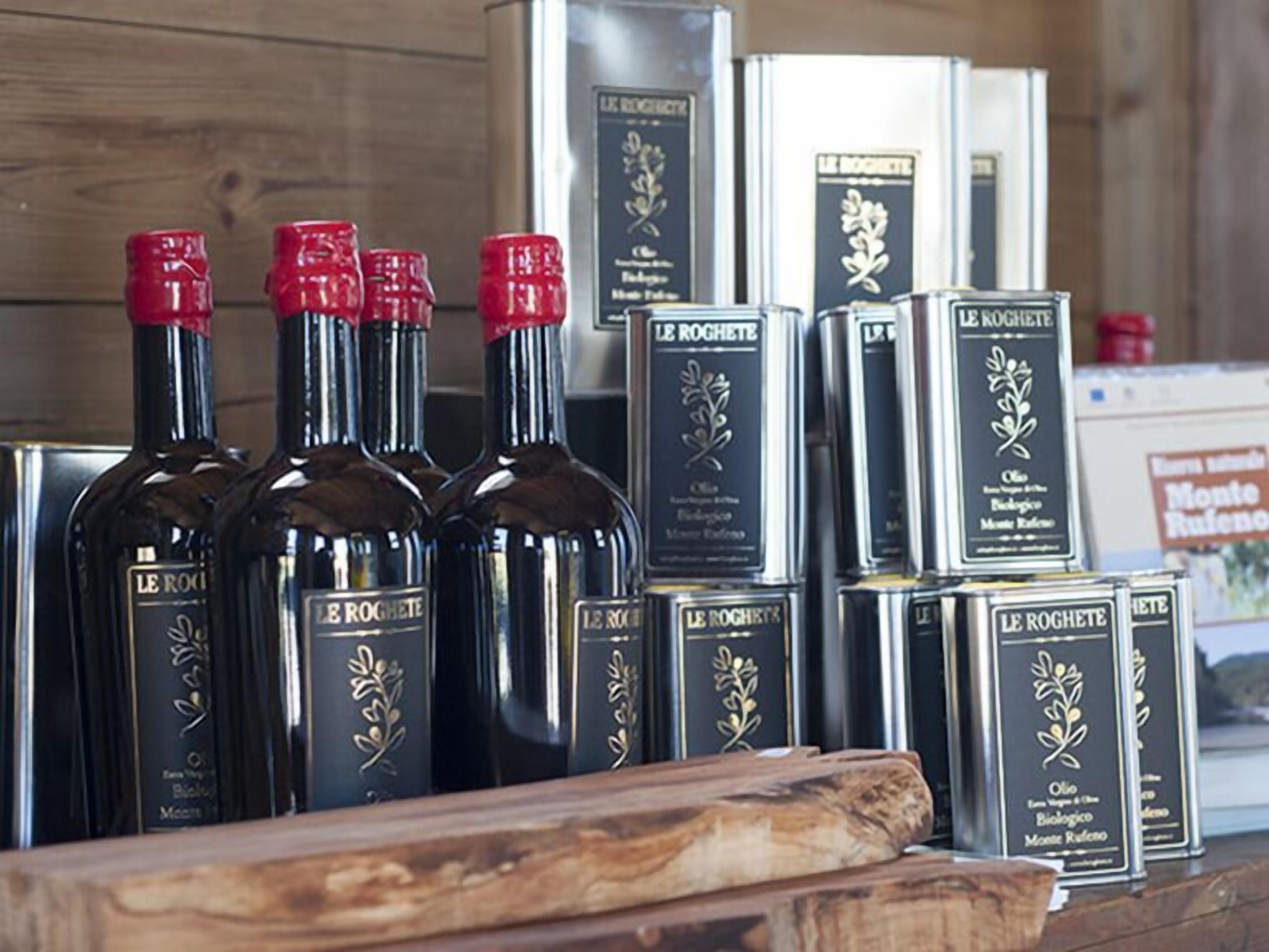 Bottiglie di olio d'oliva Le Roghete e scatole dello stesso prodotto su un piano di legno.