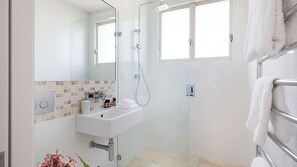 Un baño moderno con cabina de ducha de vidrio, lavabo con artículos de aseo y toallero.