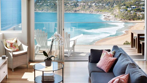 Una sala de estar moderna con un gran ventanal que da a un balcón con vista a la playa y al océano.