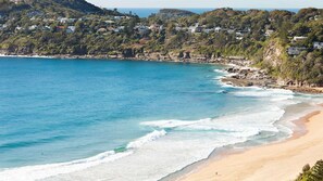 A coastal view with a sandy beach, ocean waves, and a residential area with houses on a hillside. - Palm Beach Penthouse by Contemporary Hotels (PALM BEACH)
