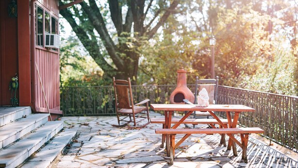 Eine Terrasse mit Steinstufen, die zu einem Holztisch und Stühlen führen, umgeben von einem Zaun und Bäumen.
