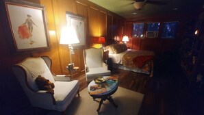 Ein gemütliches Hotelzimmer mit einem Bett, einer Sitzecke mit Sessel und Tisch, einer Lampe und einem gerahmten Bild an der Wand.