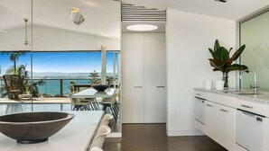 Une cuisine moderne avec vue sur la mer, un coin repas agrémenté d’un grand saladier et une plante posée sur le plan de travail.