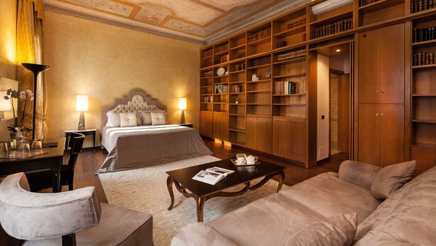 Une chambre d’hôtel dotée d’un grand lit, d’un coin salon avec une table, d’une bibliothèque et d’une armoire.
