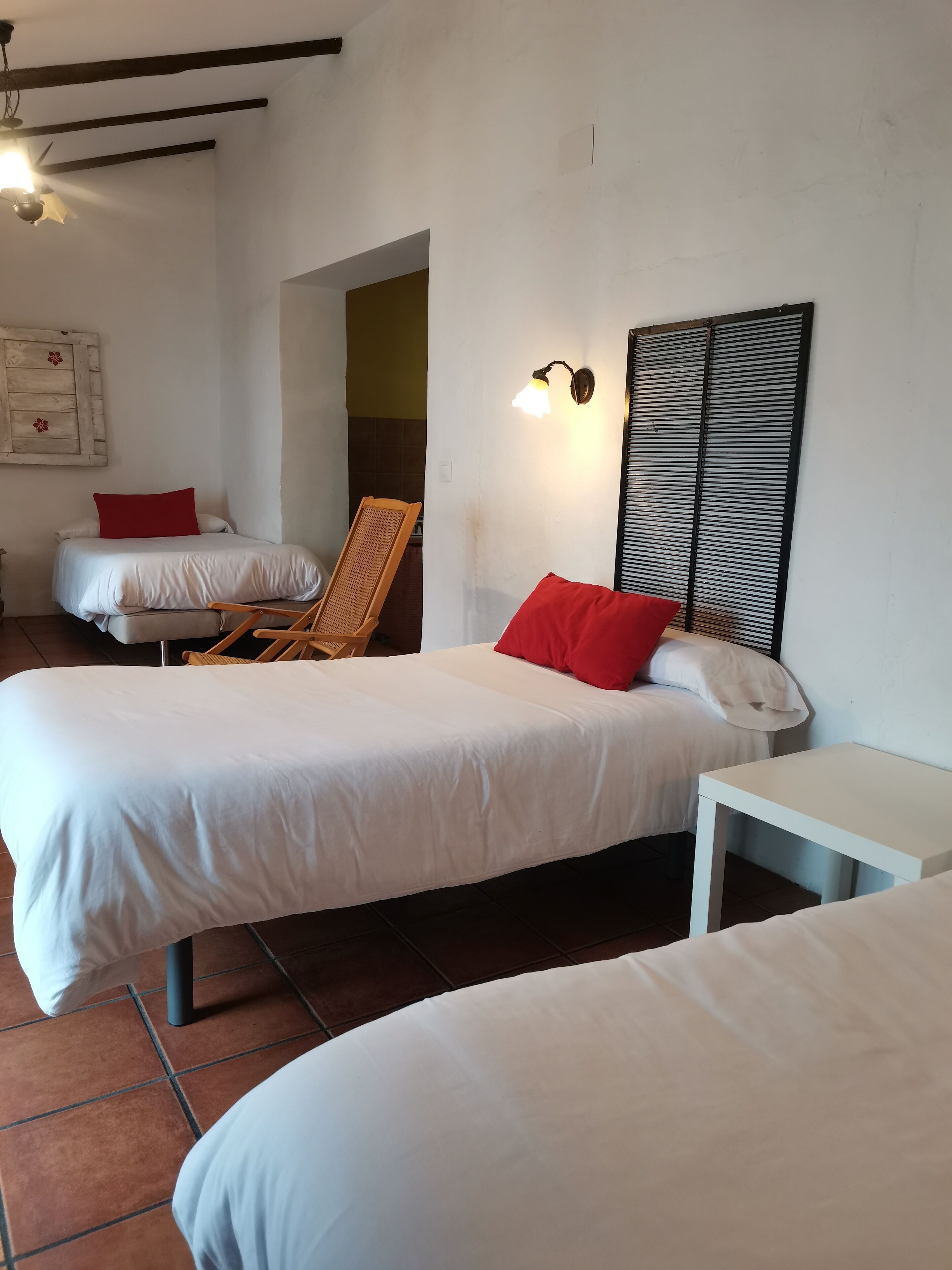 A hotel room with two beds, a small table, a chair, and a wall-mounted light fixture.