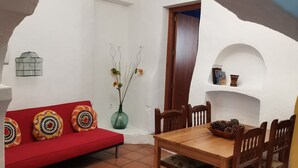 Ein Essbereich mit einem Holztisch und Stühlen, einer roten Couch mit gemusterten Kissen und einer Wandvase mit Blumen.