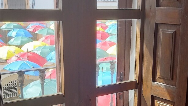 Eine Holztür mit Glasschilden, durch die sich bunte Regenschirme draußen zeigen.