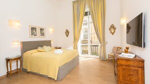 A hotel room with a bed, bedside tables, a desk, a chair, a TV, and a balcony with curtains. - Prestigious Apartments Via Barberini (Rome)