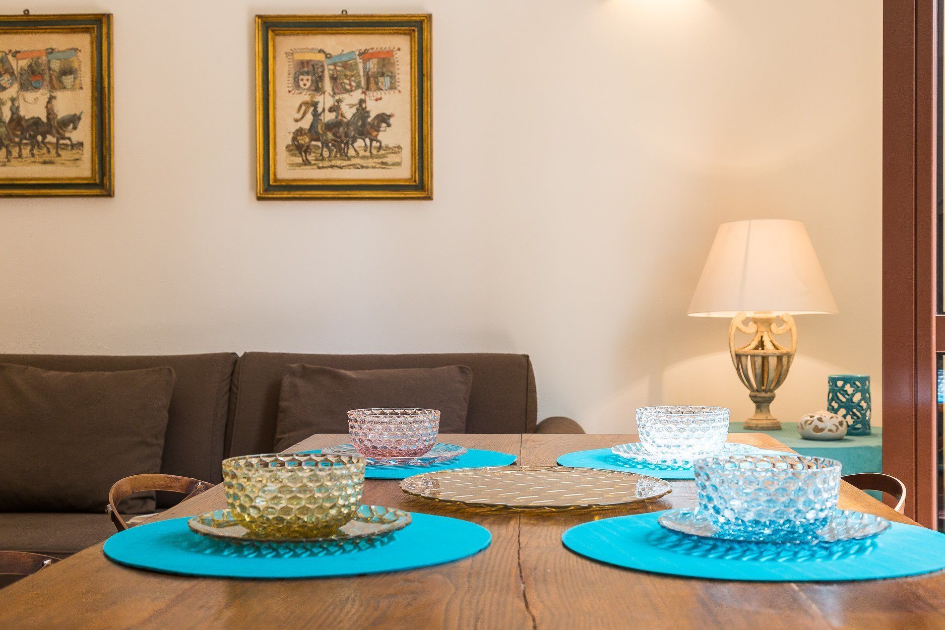 Uma mesa de jantar com jogos americanos azuis, recipientes de vidro transparentes e uma mesa de madeira.
