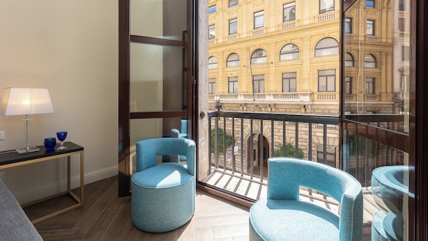 A balcony with two blue chairs, a small table with a lamp, and a view of a yellow building. - Prestigious Apartments Via Barberini (Rome)