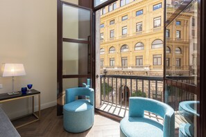 A balcony with two blue chairs, a small table with a lamp, and a view of a yellow building. - Prestigious Apartments Via Barberini (Rome)