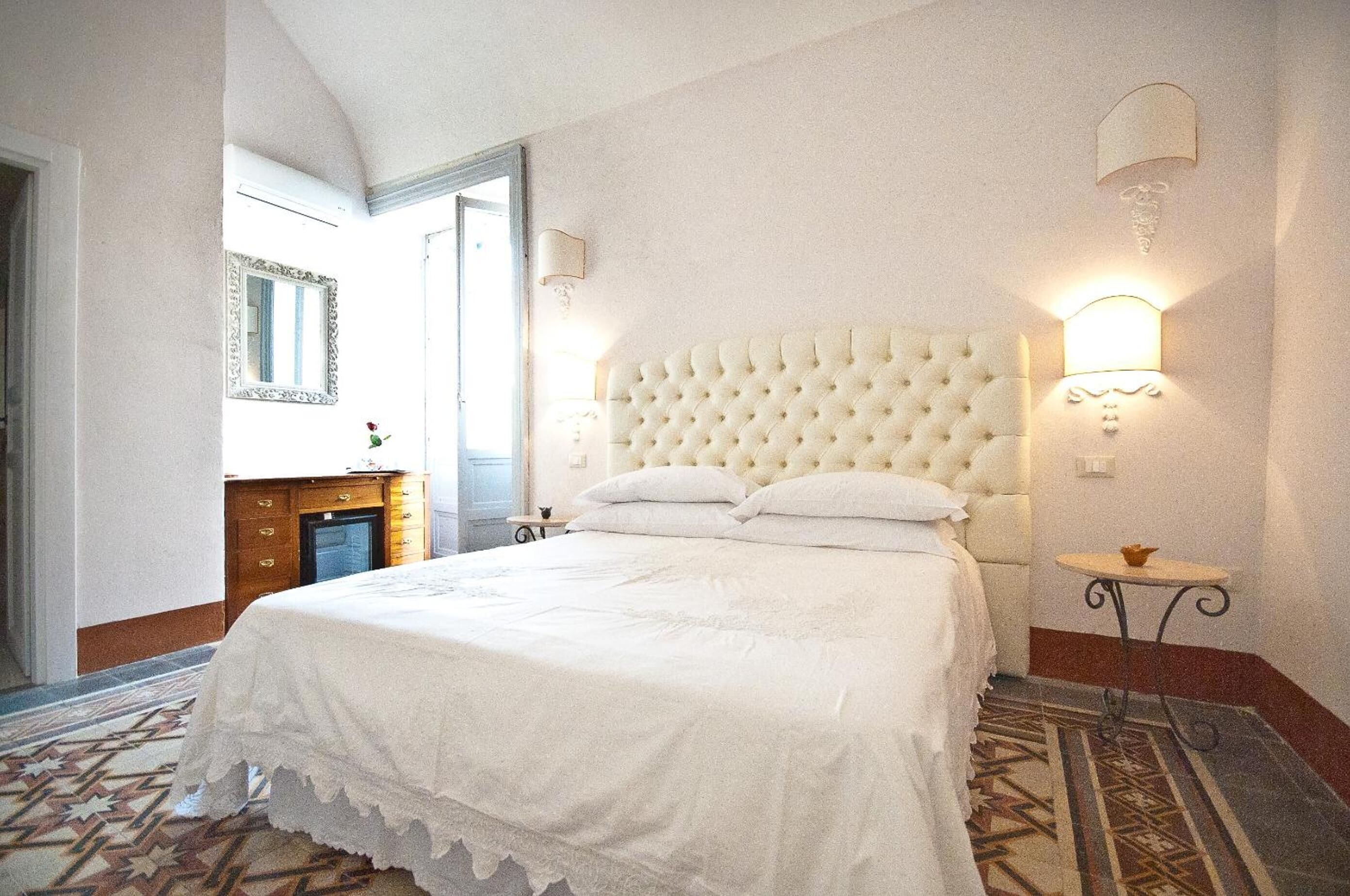 A hotel room with a large bed, a wooden dresser, a mirror, and a small table with a lamp.