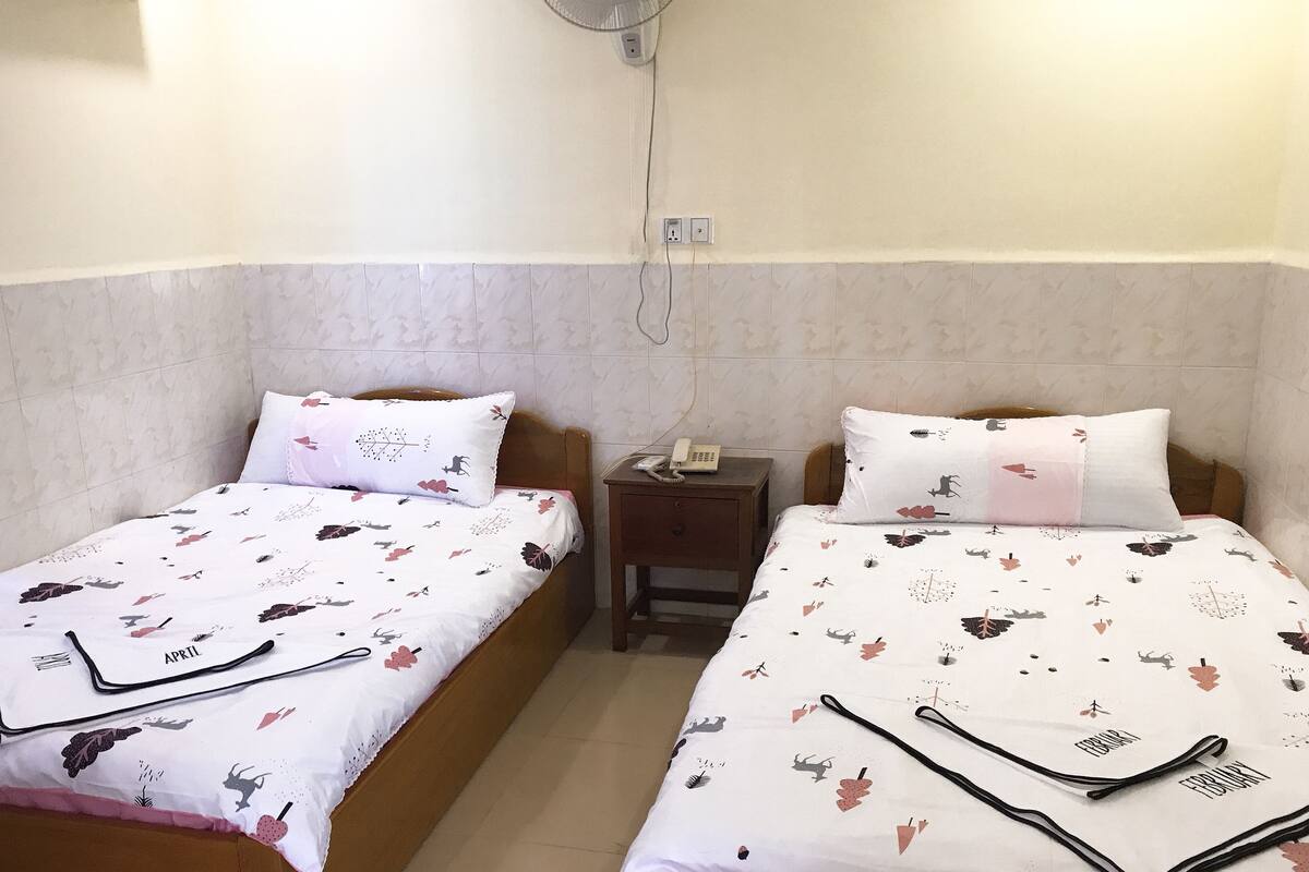 Habitació d'hotel amb dos llits, cadascun amb un estovat i coixins estampats. Hi ha una taula de nit amb un telèfon a sobre.