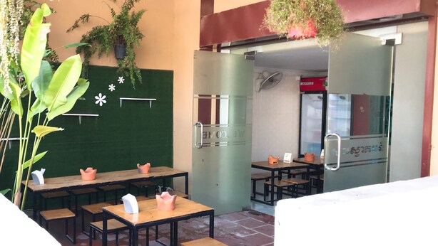 An outdoor seating area with tables and chairs, potted plants, and a green wall with decorative elements. - Mini Hotel (Phnom Penh)