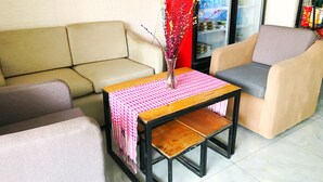 A living room with a beige sofa, a grey armchair, a wooden coffee table with a pink checkered tablecloth, and a vase with branches. - Mini Hotel (Phnom Penh)