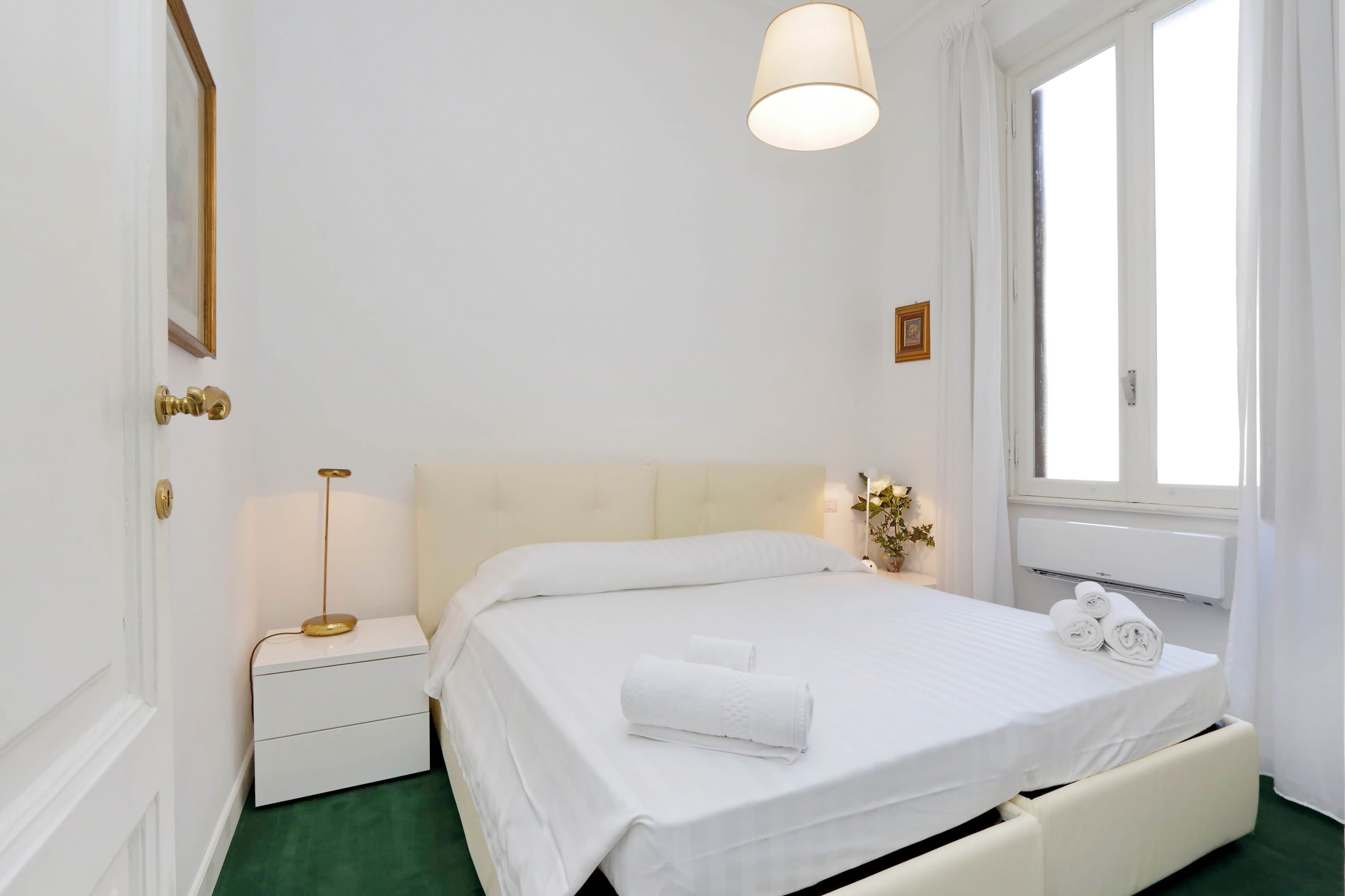 A neatly arranged bedroom with a bed, bedside table, lamp, and window.