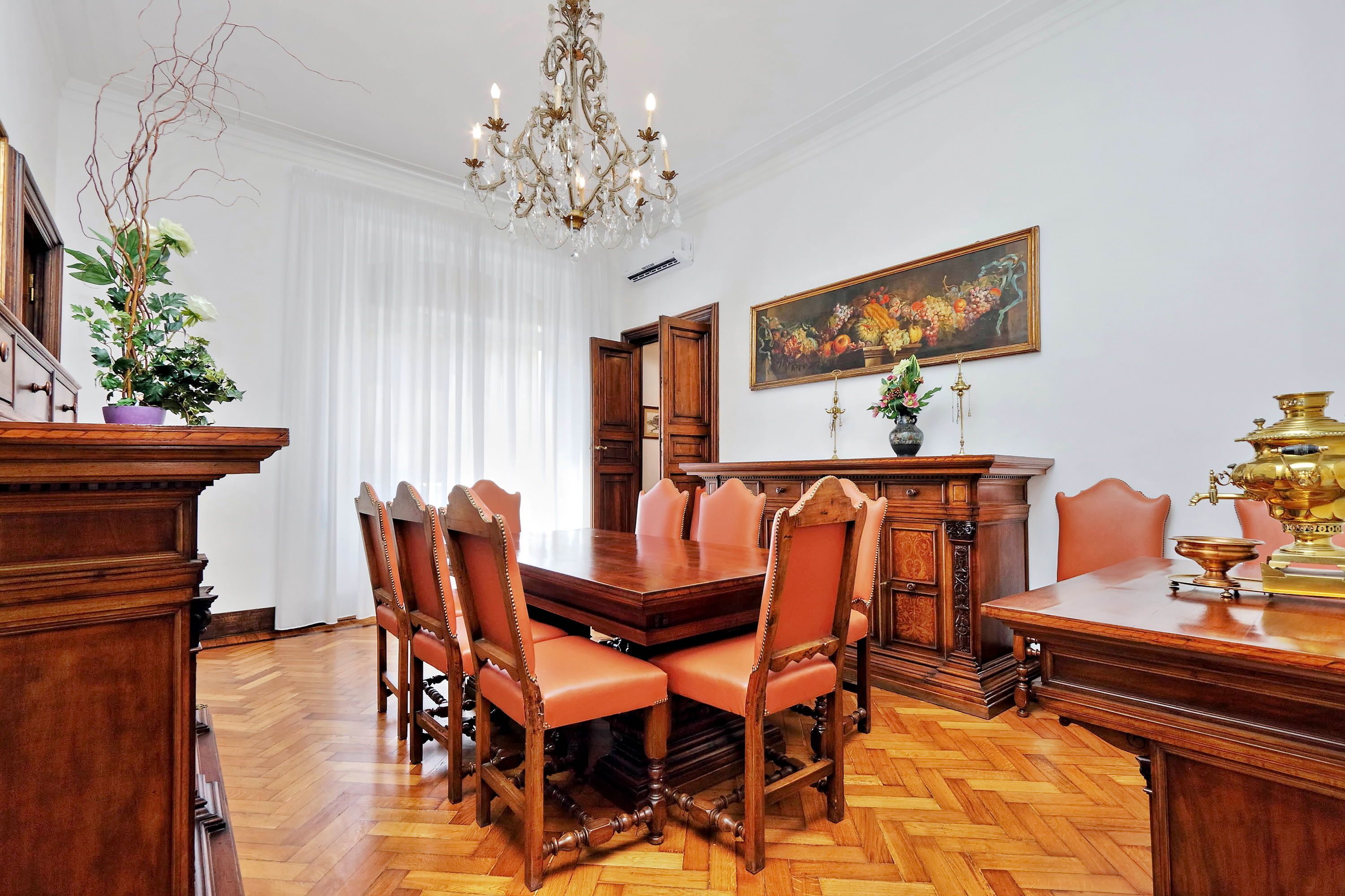 A formal dining room with a wooden table and chairs, a chandelier, and a painting on the wall.